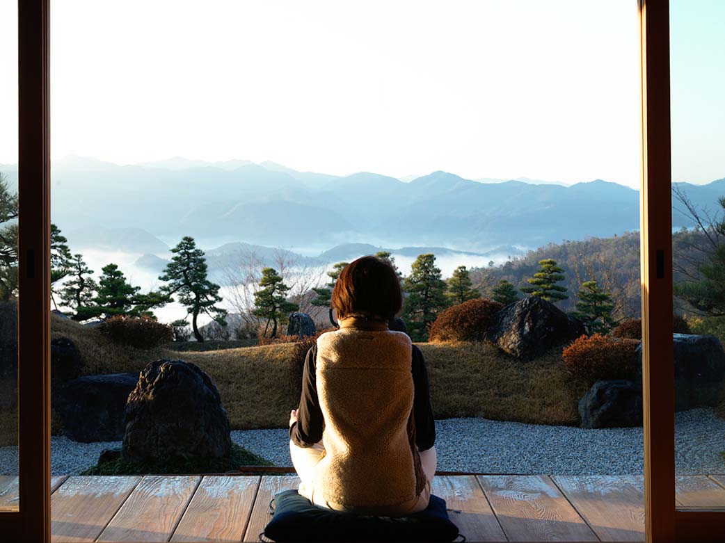 A woman on her well-being journey. She is meditating in a beautiful Japanese landscape